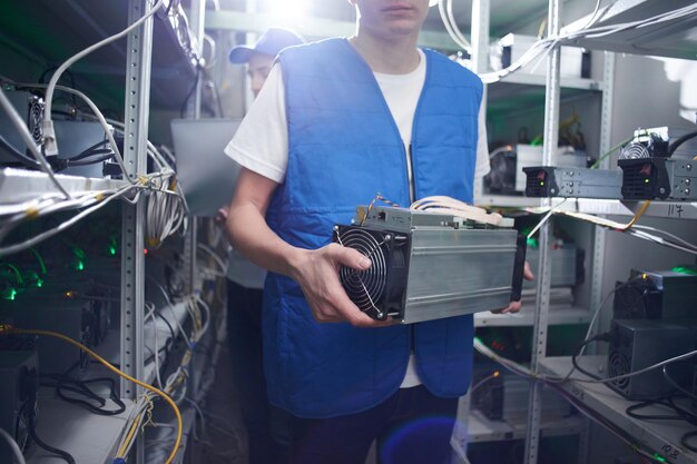 Mineração. Um homem trabalha em uma fazenda de criptomoedas. Possui equipamento de mineração de bitcoin em mãos