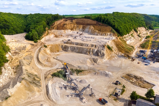 Minería a cielo abierto de materiales de piedra arenisca de construcción con excavadoras y camiones volquete en cinta transportadora.