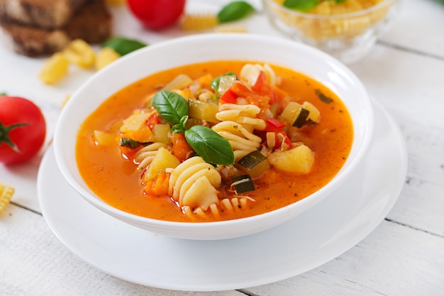 Minestrone, sopa de verduras italiana con pasta en la mesa de madera blanca