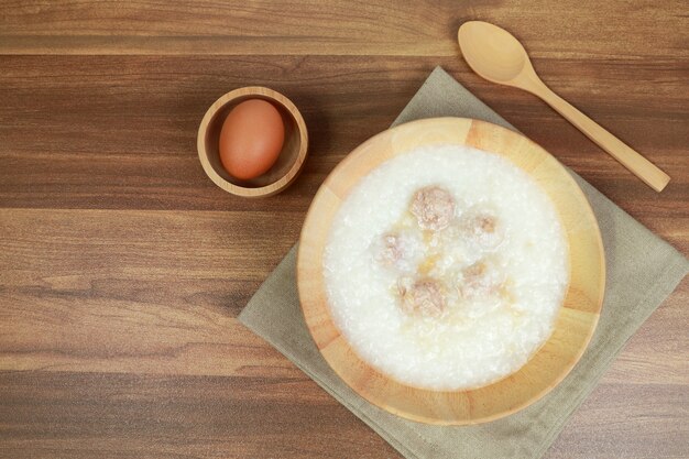 Mingau de arroz com almôndega, ovo e colher na mesa de madeira