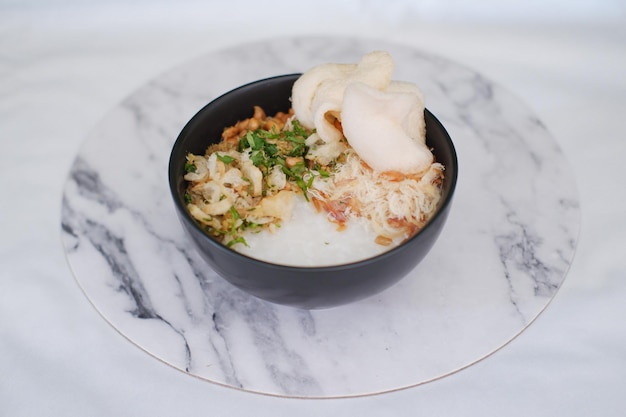Mingau de arroz com frango em tigela preta na mesa de mármore branco