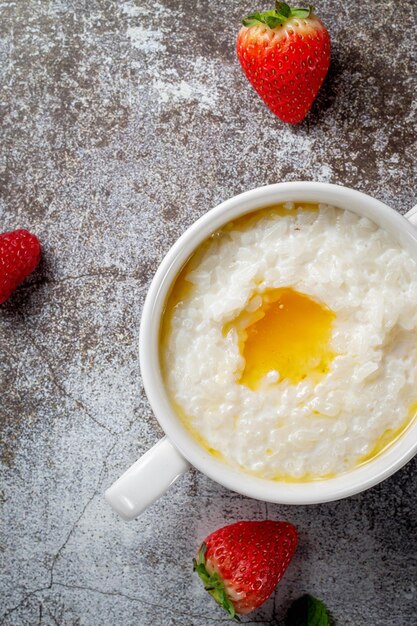 Mingau de arroz com manteiga e morangos frescos e framboesas com hortelã em um copo branco contra uma mesa de pedra cinza. um café da manhã saudável em um restaurante