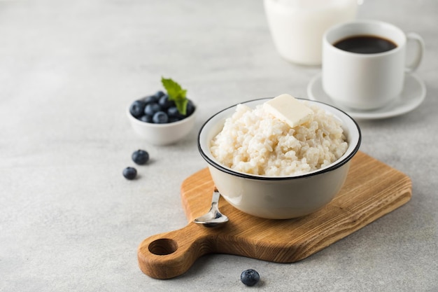 Mingau de arroz ou pudim com um pedaço de manteiga uma caneca de café e mirtilos em uma tigela Copiar espaço