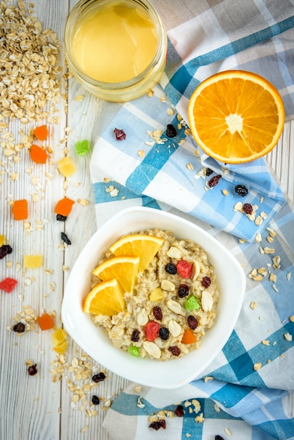 Mingau de aveia caseiro com laranja e frutas cristalizadas no espaço de madeira branco.