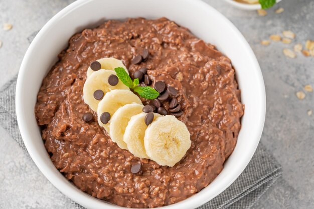 Mingau de aveia com chocolate com banana e lascas de chocolate por cima em uma tigela branca Copiar espaço
