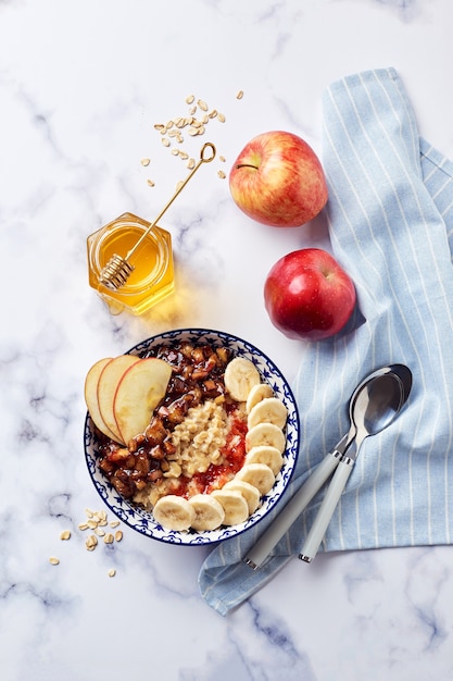 Mingau de aveia com maçãs caramelizadas com canela, banana, morangos ralados e mel na luz de fundo de mármore, vista superior.