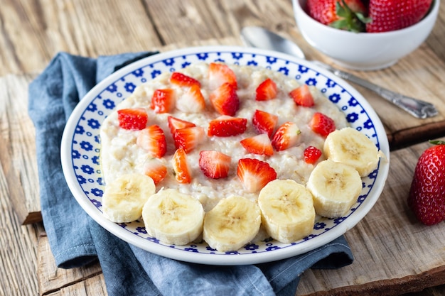 Mingau de aveia com morangos e banana na mesa rústica de madeira. Café da manhã saudável com frutas orgânicas frescas.