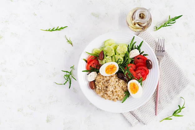 Mingau de aveia no café da manhã com salada grega de tomate, pepino, azeitonas e ovos. Alimentação saudável e equilibrada. Vista superior, disposição plana, espaço de cópia
