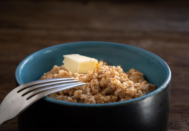 Mingau de cevada em uma tigela de cerâmica e um garfo em uma mesa de madeira. Comida caseira.