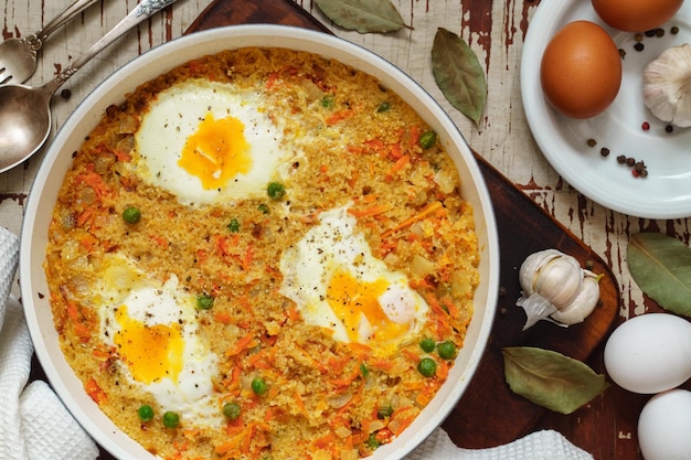 Mingau de trigo com legumes e ovos em uma frigideira branca