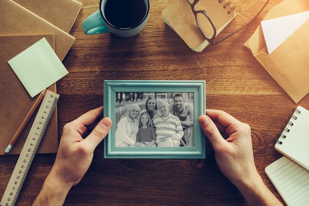 Minha família é minha inspiração. Close-up de um homem segurando uma foto de sua família sobre uma mesa de madeira com várias coisas da chancelaria por perto