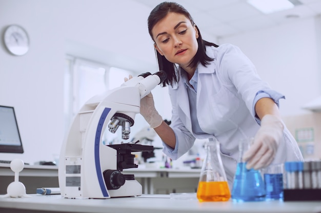 Minhas responsabilidades. cientista linda e habilidosa trabalhando com um microscópio e tocando os tubos