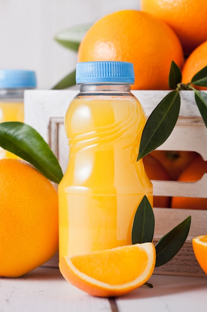 Mini botellas de plástico de jugo de naranja fresco orgánico con naranjas crudas en caja de madera blanca