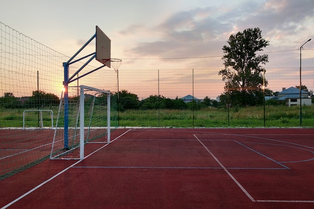 Mini cancha de fútbol y baloncesto al aire libre con portón de pelota y canasta rodeada con una alta valla protectora.