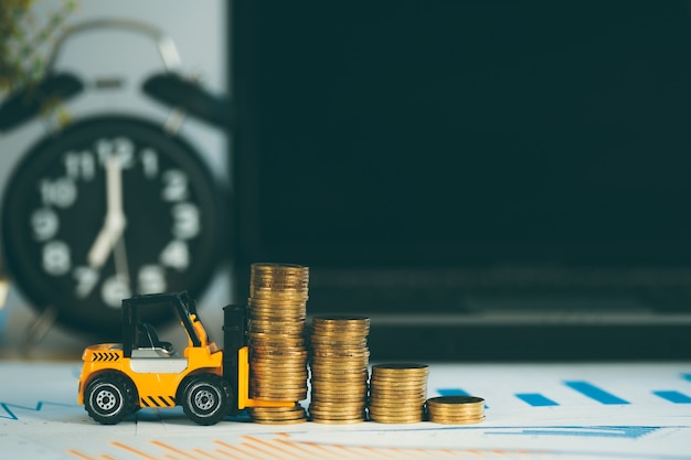 Mini carretilla elevadora en miniatura con pila de monedas en la mesa de trabajo