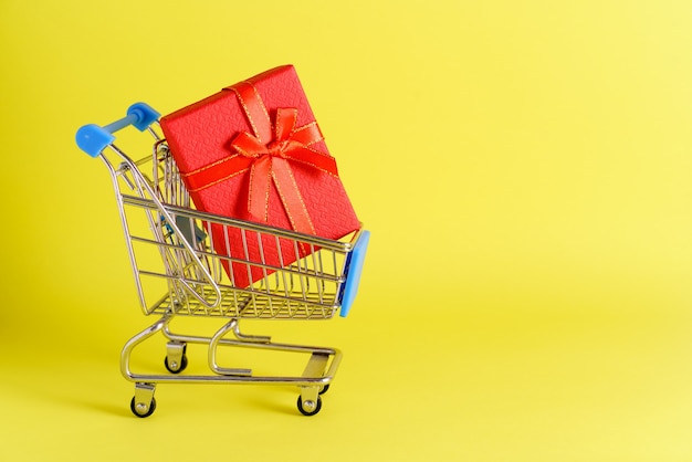 Mini carrinho com pequena caixa de presente vermelha no conceito de compras de fundo amarelo nas lojas e no ...