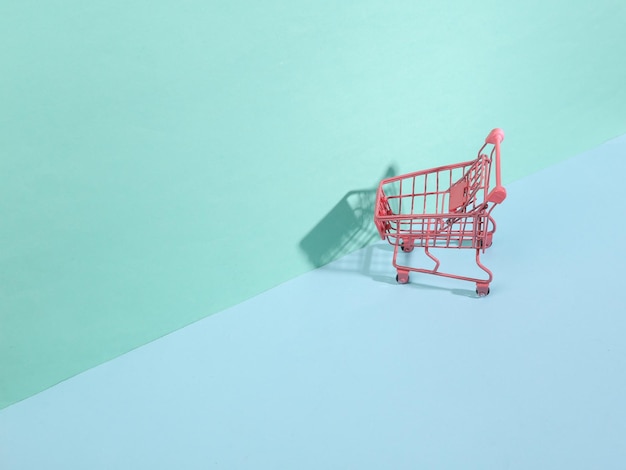 Mini carrinho de compras rosa sobre fundo azul com sombras da moda Layout criativo Natureza morta minimalista