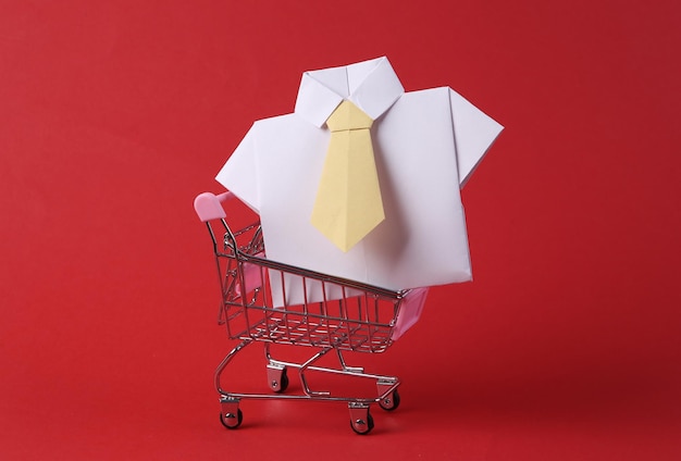 Mini carrito de compras con camiseta de origami sobre fondo rojo.