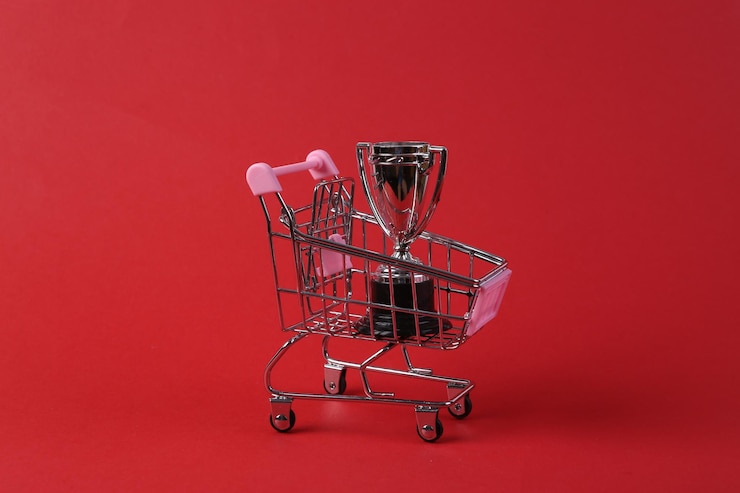 Foto mini carrito de compras con copa ganador sobre fondo rojo.