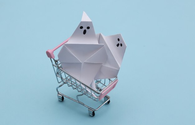 Mini carrito de compras con fantasmas de origami sobre fondo azul. Tema de halloween