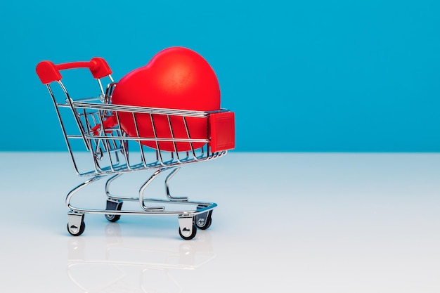 Un mini carrito de compras con forma de corazón rojo sobre un fondo azul de estudio Día de San Valentín Concepto de amor El concepto de preservación de la salud