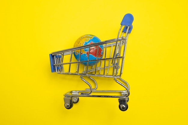 Mini carrito de compras con globo sobre fondo amarillo Globo terráqueo en el mini carrito