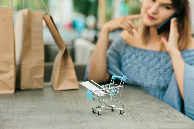 Foto mini carrito de compras en línea con un primer plano de tarjeta bancaria con fondo borroso de joven adicta a las compras