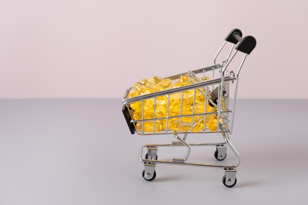 Mini carrito de compras con pastillas y tabletas sobre fondo gris