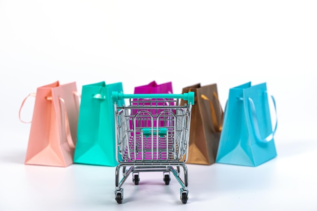 mini carrito de compras vacío y bolsas de papel coloridas aisladas en una maqueta de fondo brillante para el diseño