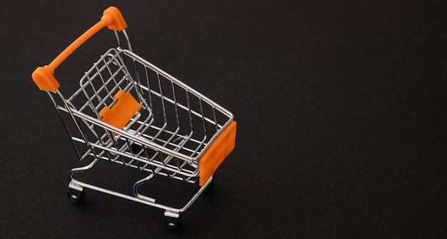 Mini carrito de supermercado naranja sobre fondo negro Concepto de compras