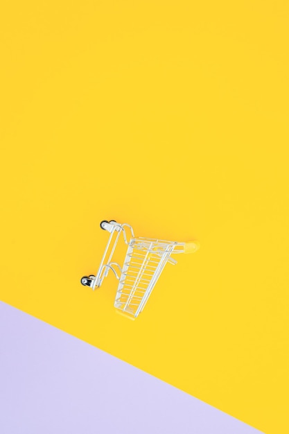 Foto mini carrito de supermercado sobre fondo amarillo violeta