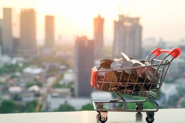 Mini carro de la compra o carro de supermercado con monedas de baht en el fondo de la ciudad de desenfoque