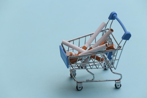 Mini carro de supermercado con cigarrillos sobre fondo azul.