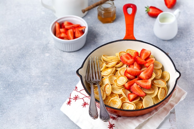 Mini cereal panqueque blanco con fresas en una sartén para desayunar en la superficie gris. Vista superior.