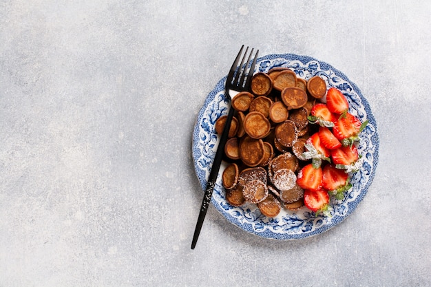 Mini cereal de panqueques de chocolate con fresas para el desayuno en la mesa de hormigón gris