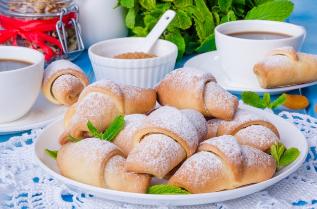 Mini croissants con albaricoques secos, higos y nueces en un plato con una taza de café.