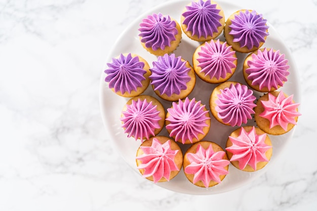 Mini cupcakes de baunilha recém-assados com cobertura de creme de manteiga rosa ombre em um suporte de bolo branco