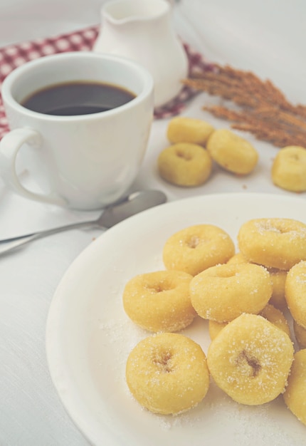 Mini Donuts auf weißem Teller und eine Tasse Kaffee.