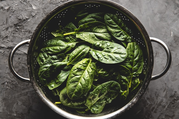 Foto mini espinacas frescas en un colador sobre la vieja mesa de hormigón. comida sana, producto ecológico. vegano