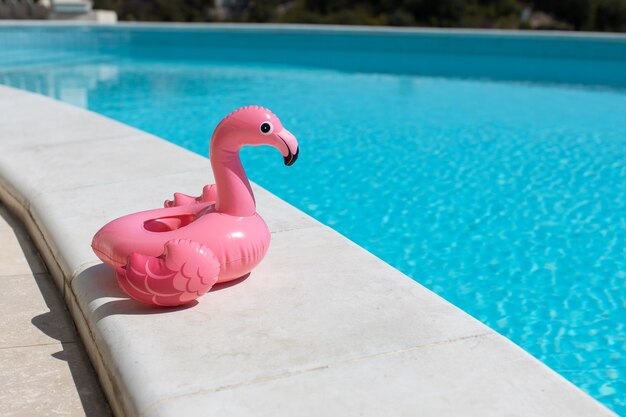Mini flamenco rosa inflable, puesto de cócteles cerca de la piscina en un día soleado, copie el espacio. Concepto de vacaciones de verano, entretenimiento, agua, aire, tomar el sol, salud. Vista lateral. Horizontal.