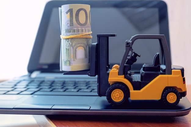 Mini-Gabelstapler laden Stapel von Banknoten auf Laptop-Tastatur. Logistik, Transport, Managementideen, Geschäftskonzept der Industrie.