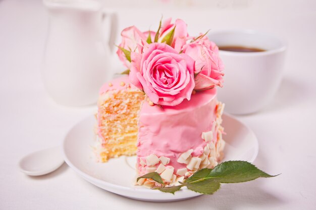 Mini kleiner Kuchen mit rosa Glasur, schönen Rosen, Tasse Kaffee auf dem weißen Tisch.