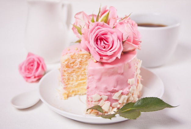 Mini kleiner Kuchen mit rosa Glasur, schönen Rosen, Tasse Kaffee, Geschenkbox auf dem weißen Tisch.