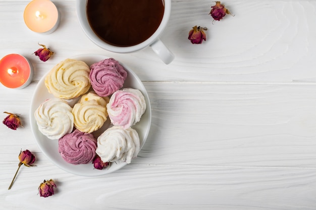 Mini Marshmallows mit verschiedenen Aromen auf einem weißen Teller mit einer Tasse heißer Schokolade