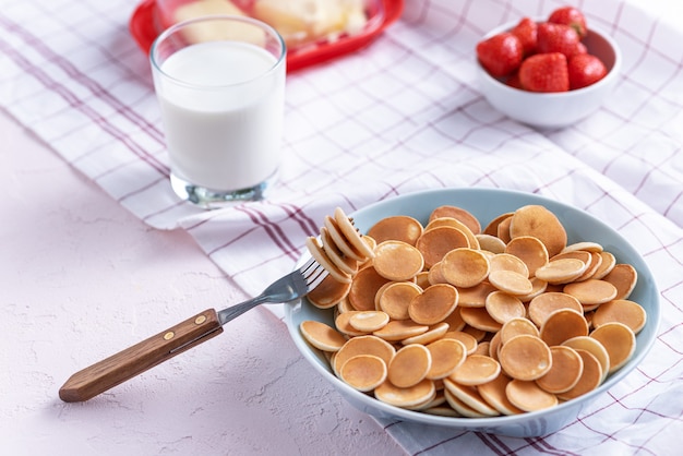 Mini panquecas de cereal em uma tigela azul com garfo, morangos e copo de leite branco