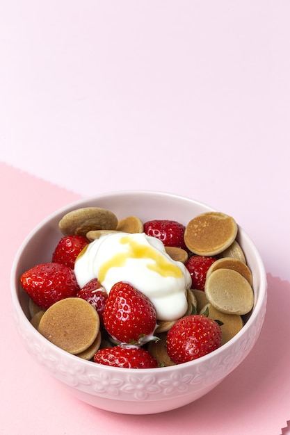 Mini panqueque de cereales caseros con yogur, miel y fresas en mesa de colores.