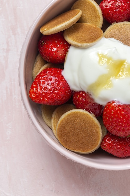 Mini panqueque de cereales caseros con yogur, miel y fresas en mesa de colores.