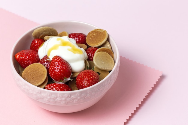 Mini panqueque de cereales caseros con yogur, miel y fresas en mesa de colores.