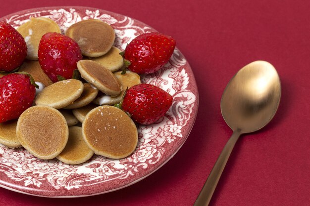 Mini panqueque de cereales caseros con yogur, miel y fresas en mesa de colores.