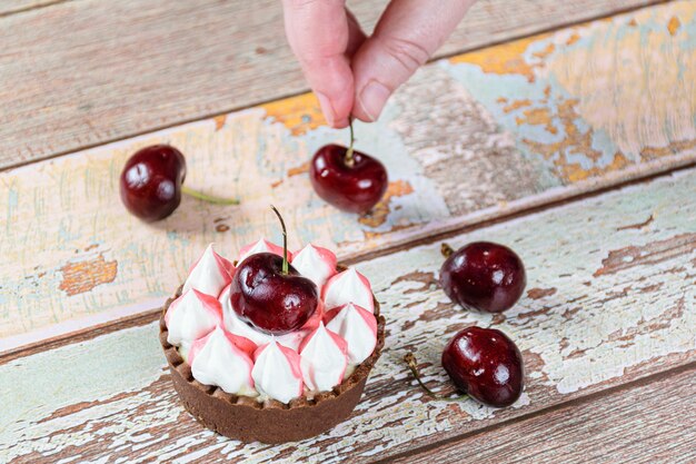 Mini pastel de chocolate con ganache de chocolate, cubierto con crema batida y cereza. Al fondo, repostero colocando cerezas.